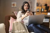 Woman sat on a sofa with a laptop using her mobile phone