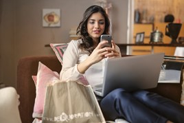 Woman sat on a sofa with a laptop using her mobile phone