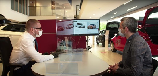 Wearing masks, a car salesman presents a new Vauxhall to a car buyer